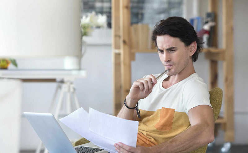 student myśli trzymając laptopa i papiery
