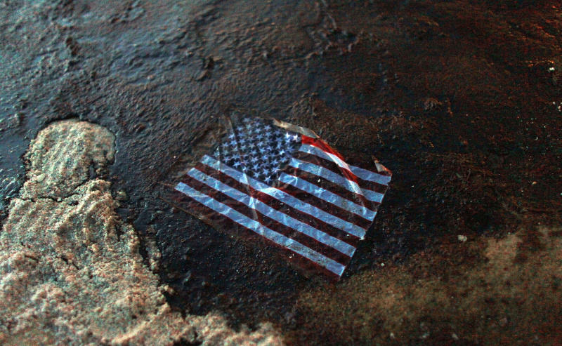 Amerikas karogs atrodas naftas plankumā, kas 2010. gada 4. jūlijā Gulf Shores, Alabamas štatā, tika izskalots krastā no naftas noplūdes Deepwater Horizon Meksikas līcī.