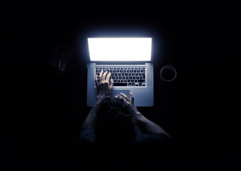 Kobieta korzystająca z laptopa w ciemności z rękami oświetlonymi przez ekran komputera na czarnym tle