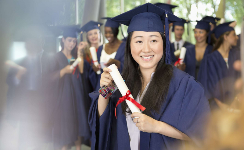 Portret uśmiechniętej studentki w sukni ukończenia szkoły trzymającej dyplom