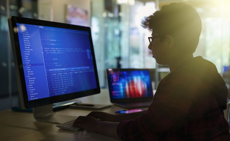 Estudante de menino programando no computador na sala de aula escura