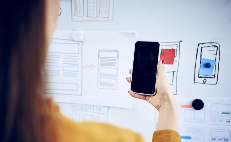 Kvinne holder smarttelefon og ser på webdesignideer på tavlen