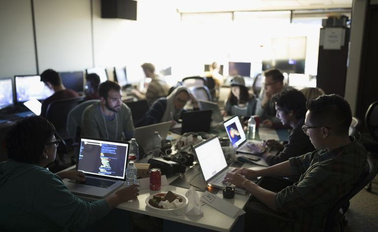 Hackers trabajando en un hackathon en computadoras portátiles en una oficina oscura
