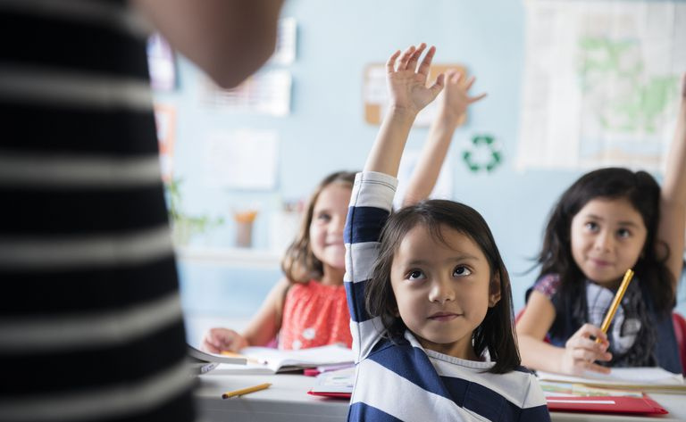 Kleines Mädchen, das im Klassenzimmer die Hand hebt