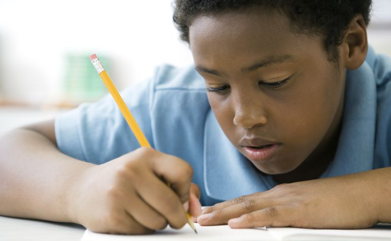 5 年生の男子生徒が鉛筆を使ってノートに書き込んでいます