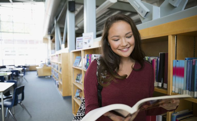 Smilende ungdomsskoleelev leser bok i biblioteket