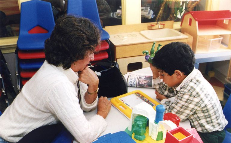 Ein Lehrer, der mit einem Schüler arbeitet, während beide ein Lehrmittel auf einem Tisch studieren.