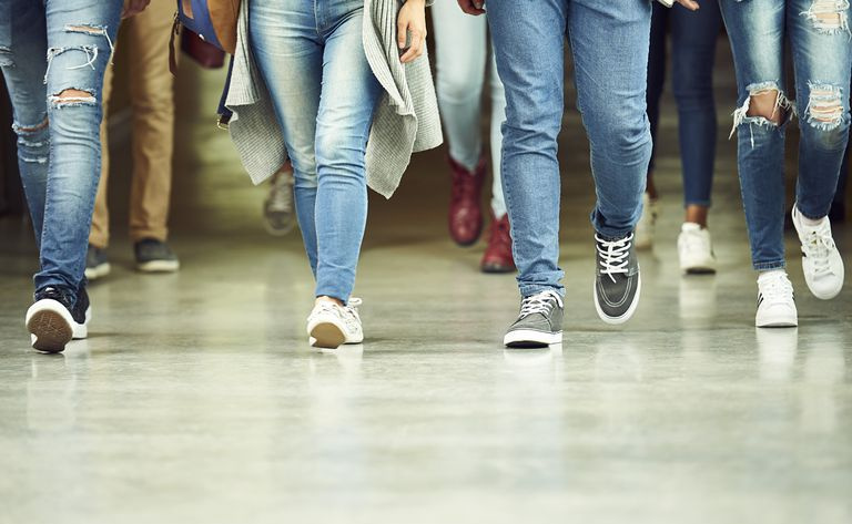 Les jambes de quatre étudiants portant des jeans marchant dans un couloir