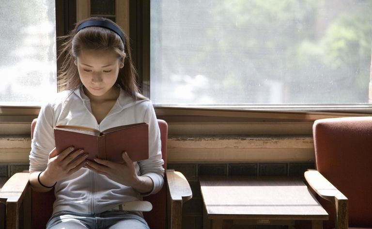 Giovane donna seduta in poltrona, libro di lettura