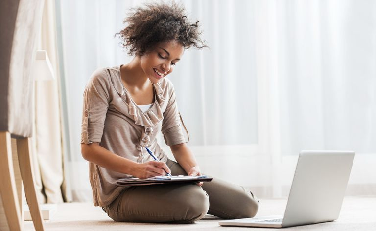 Frau schreibt auf Papier vor Laptop