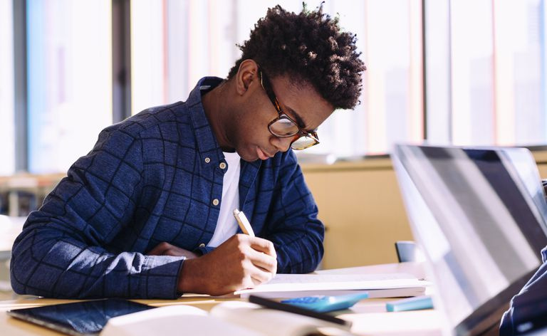 Studente che scrive seduto a tavola in biblioteca