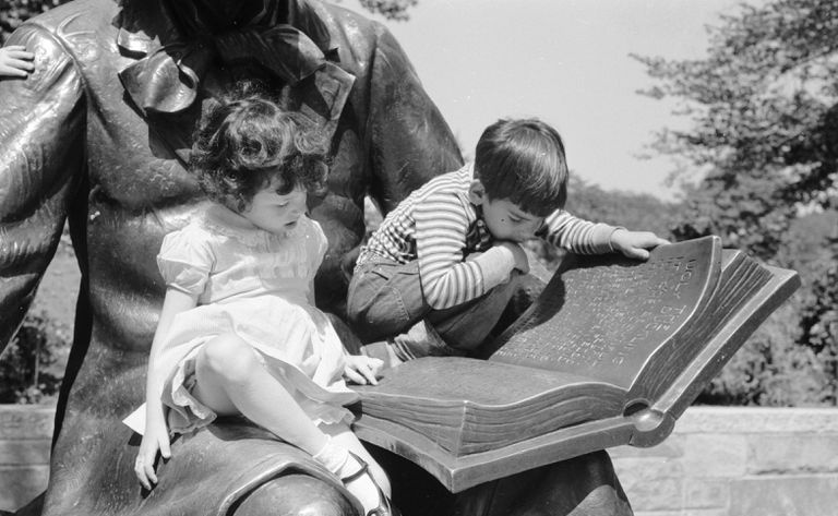 Dve deti sediace na soche Hansa Christiana Andersena čítajúceho knihu, čiernobiela fotografia.