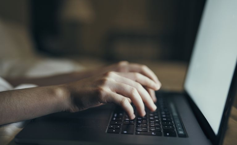 Hendene til en kaukasisk kvinne som skriver på bærbar PC i sengen