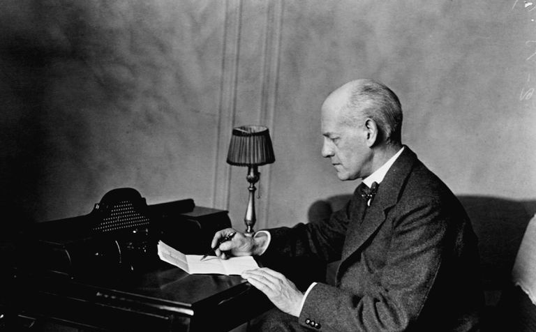 John Galsworthy escrevendo com caneta e papel em uma mesa