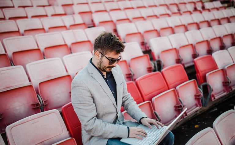 Mann jobber på en bærbar datamaskin på et stadion