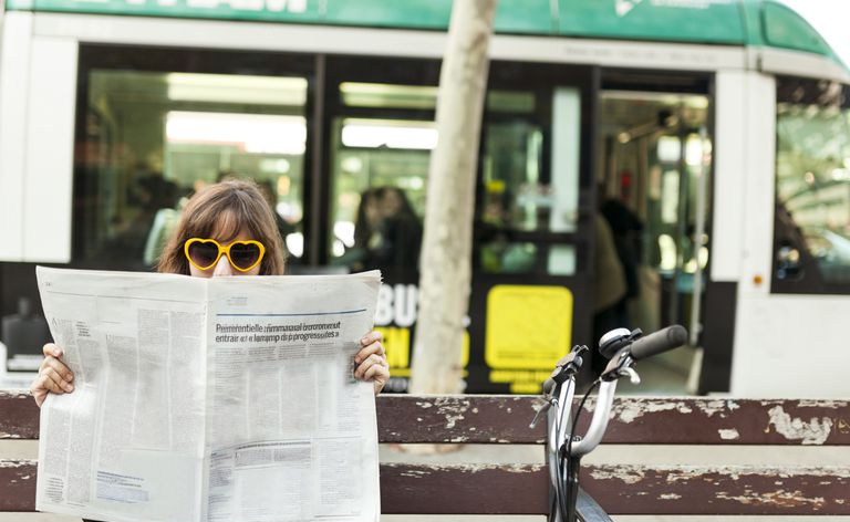 Donna che indossa occhiali da sole divertenti che legge il giornale sulla panchina della città