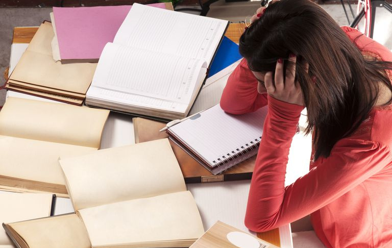Étudiante frustrée par les livres couvrant sa table