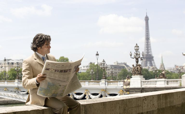 Mann som leser en fransk avis i Paris med Eiffeltårnet i bakgrunnen.