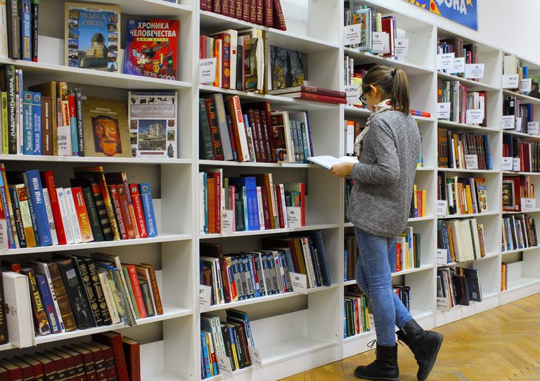 Giovane donna che passa in rassegna gli scaffali di una biblioteca.