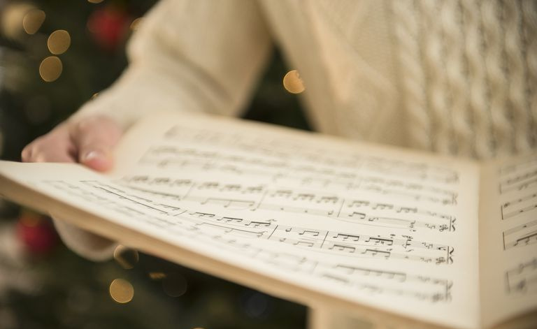 Osoba stojąca przed choinką trzyma nuty