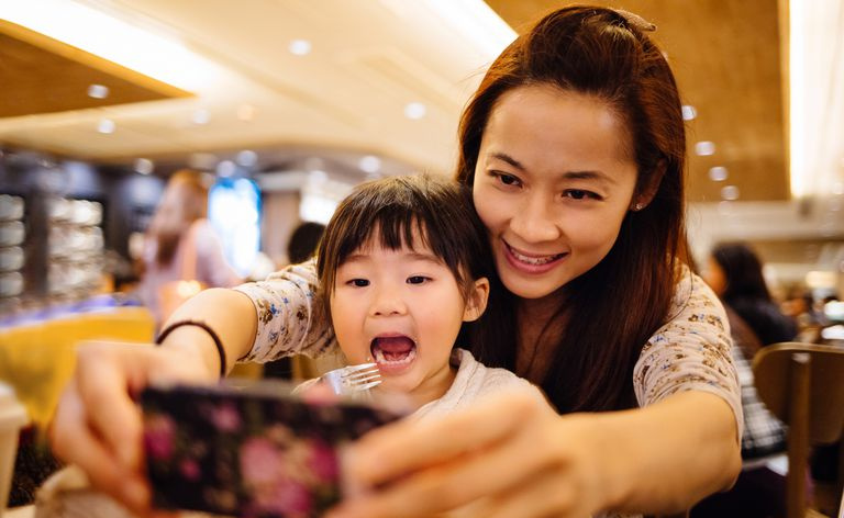 Mamma e bambina che prendono selfie con gioia nella caffetteria
