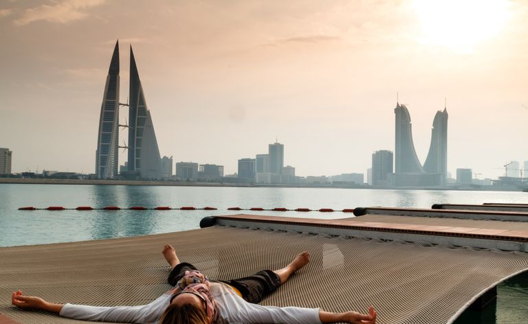 Una persona está tirada en una red en Pier Against Sky con vistas a un paisaje urbano de Bahrein