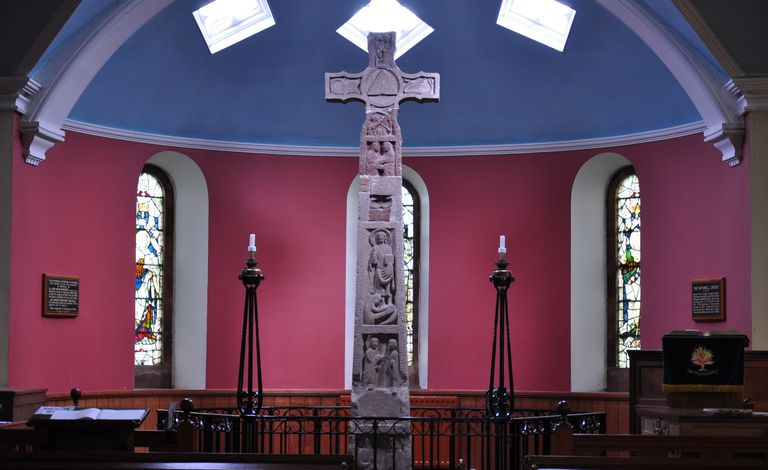 Ein kunstvoll geschnitztes Steinkreuz in der Mitte eines Kirchengebäudes mit Kuppel.