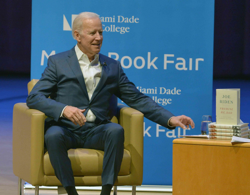 Joe Biden sentado en una silla frente a un fondo azul, con una pila de libros a su lado
