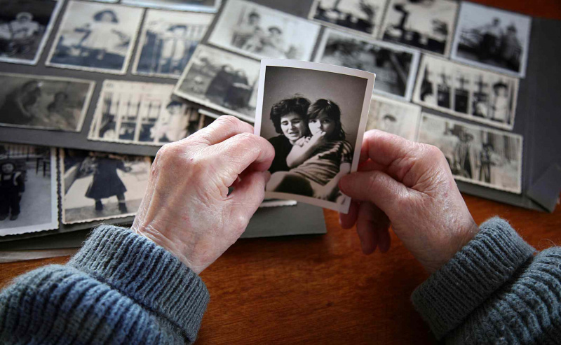 Novecojušas rokas, kas strādā, lai saglabātu vecās ģimenes fotogrāfijas bezskābes fotoalbumos