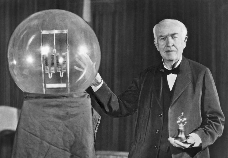 Thomas Edison stoi z dużą żarówką.
