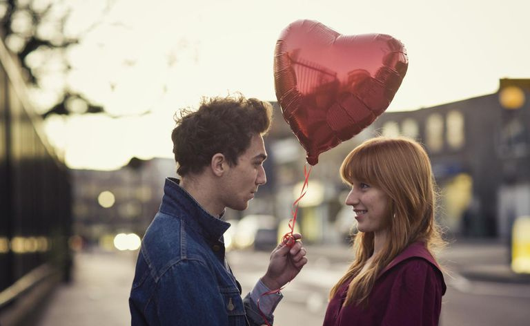 Couple avec ballon en forme de cœur se regardant au crépuscule.