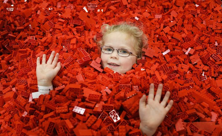 ręce i twarz dziecka w okularach wystają z morza czerwonych klocków LEGO