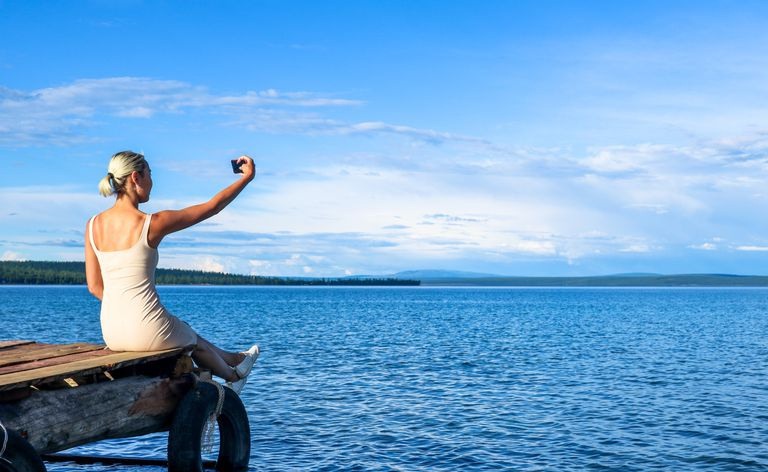 Femme assise sur un quai prenant un selfie.
