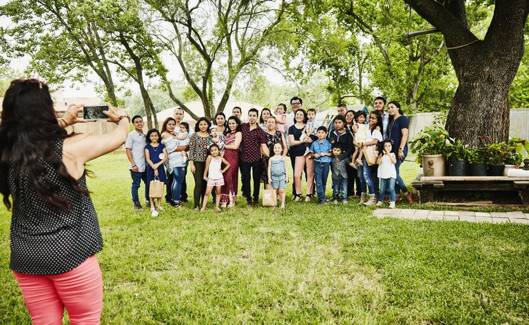 Kvinne tar bilde av smilende familie i flere generasjoner som samles til bursdagsfest i bakgården