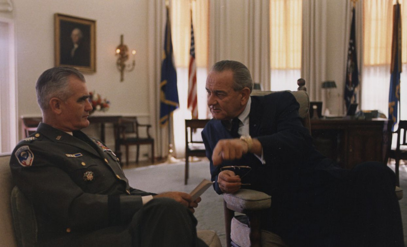 El General William Westmoreland, en uniforme del Ejército de EE. UU. y sentado, habla con el Presidente Lyndon B. Johnson en la Oficina Oval.