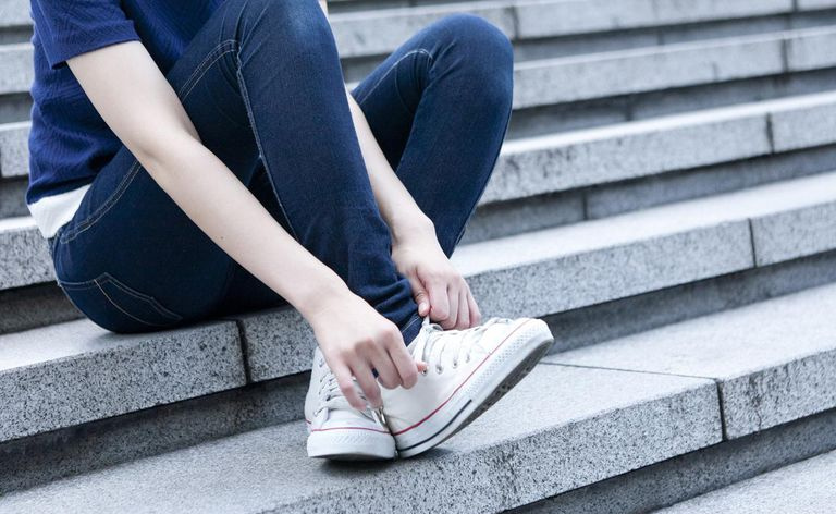 Junge Frau sitzt auf Stufen und bindet Schnürsenkel