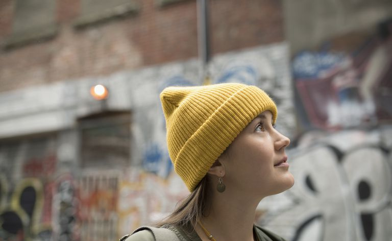 Nysgjerrig ung kvinne med gul strømpehette ser opp på urban gate