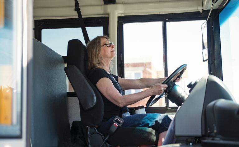 Retrato de mulher madura dirigindo um ônibus escolar.