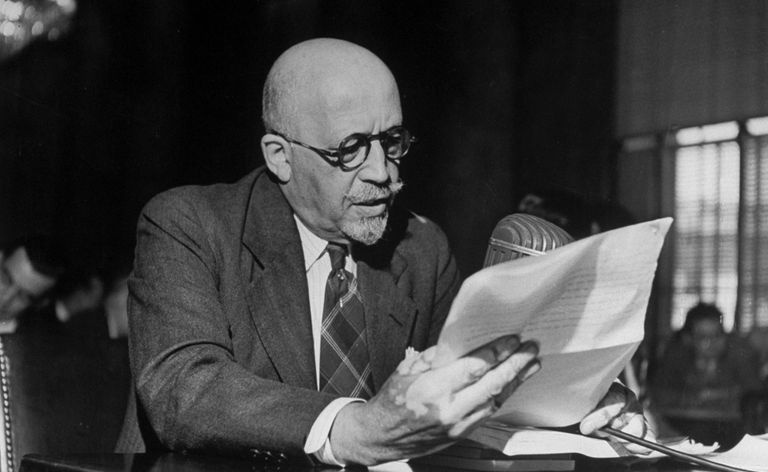 W. E. B. DuBois iført briller, sittende ved et bord og ser på papirarbeid