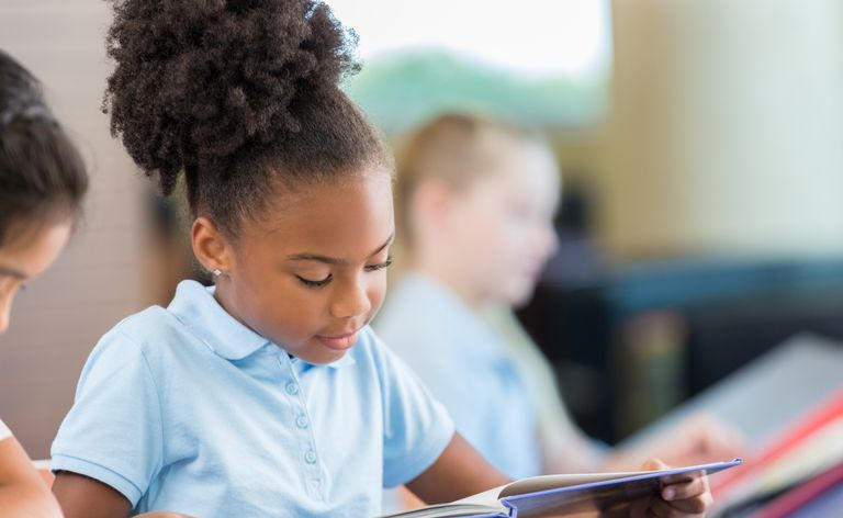 Adorável garota afro-americana lendo livros na biblioteca da escola