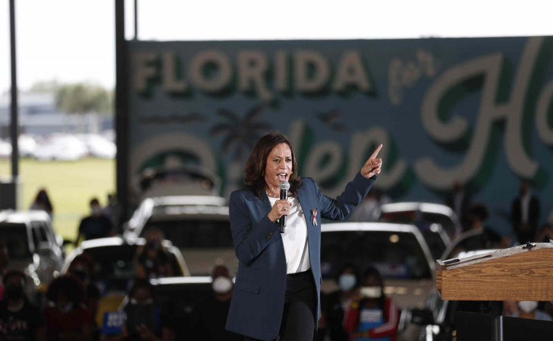 Kamala Harris snakker i en mikrofon og peker finger mens han står på en scene omgitt av biler og publikummere i Florida