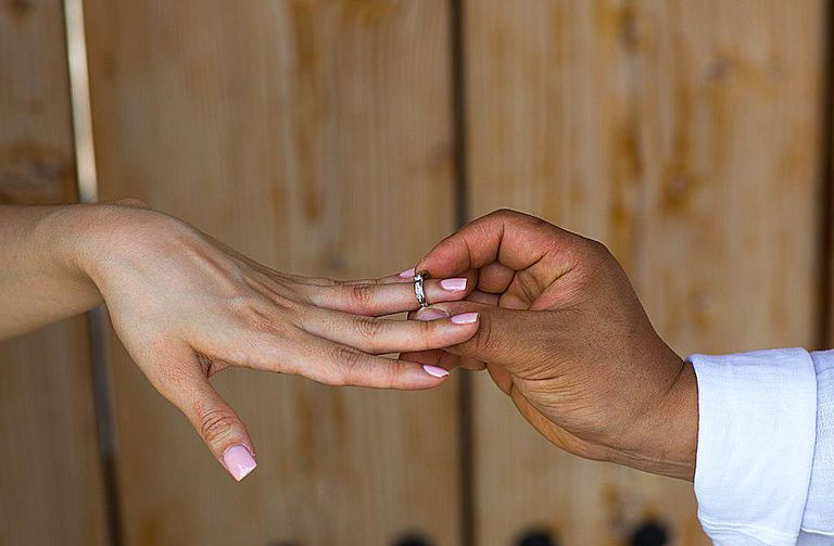 A mão de um homem inserindo um anel de casamento no dedo de uma mulher.