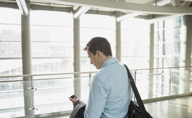 Biznesmen trzyma teczkę i wysyła SMS-y ze smartfona
