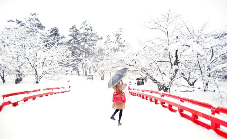 Uma mulher de pé em uma ponte coberta de neve com árvores ao redor.