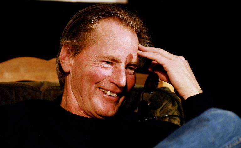 Sam Shepard w dżinsach i czarnej koszuli, z dłonią dotykającą czoła