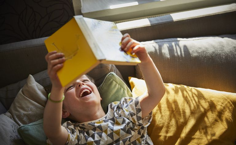 Mittelschulkind legt sich laut lachend hin, während es ein Buch liest.