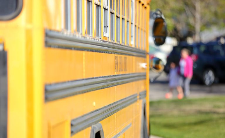 Madre e bambino che camminano verso lo scuolabus in una giornata di sole.