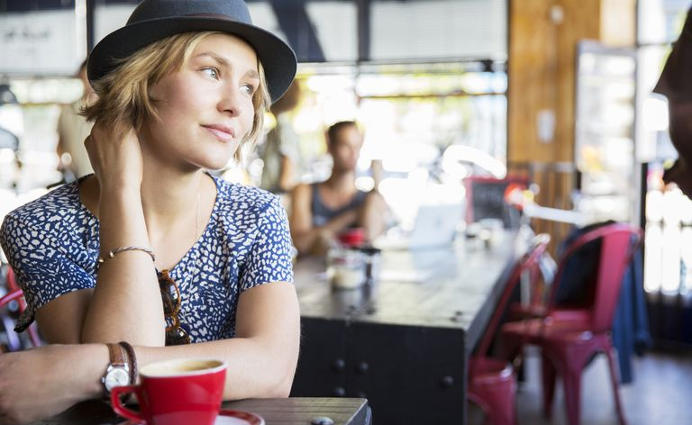 Nachdenkliche Frau mit Hut und Kaffee, die im Café wegschaut