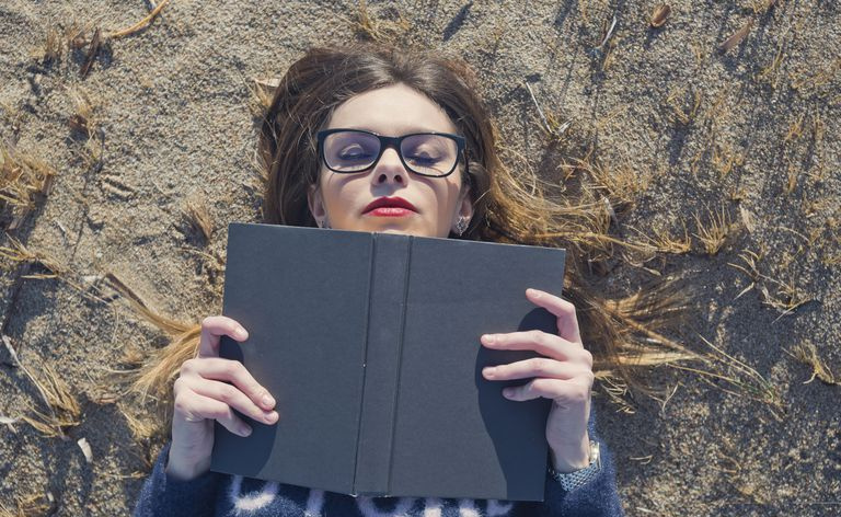Foto de uma jovem lendo um livro enquanto estava deitada na praia