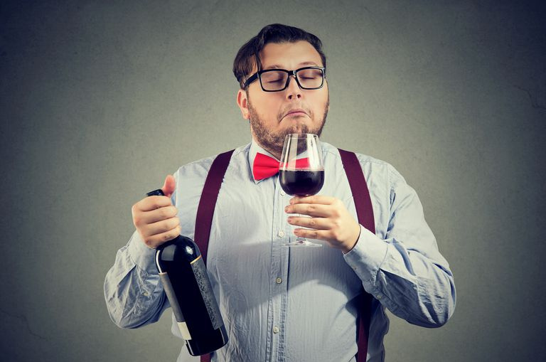 En snopet sommelier i sløyfe og hornglass lukter et glass vin
